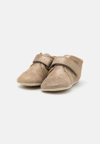 Zapatos de bebé de ante suave de color beige con una cinta de Velcro, punta redondeada y soporte acolchado en el tobillo. Presentan detalles de costura a lo largo de las costuras.