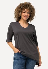 Dunkelgraues V-Ausschnitt T-Shirt mit kurzen Ärmeln, glatter Textur, lässigem Schnitt und leicht längerem Rückensaum. Kombiniert mit blauen Jeans.