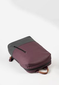 Zaino con base viola e parte superiore grigia, dotato di una tasca frontale con zip, texture liscia e manico accentato in pelle marrone.