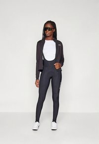 Czarna kurtka rowerowa na białej bluzce, zestawiona z czarnymi legginsami na pełną długość z białymi akcentami oraz białymi butami sportowymi.