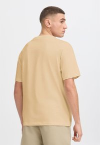Beige short-sleeve t-shirt with a crew neck, made from lightweight fabric, featuring a relaxed fit and smooth texture. No visible logos.