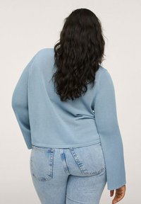 Jasnoniebieski dziany sweter z długimi, prążkowatymi rękawami, w zestawie z dopasowanymi jasnoniebieskimi dżinsami. Widoczna faktura materiału.