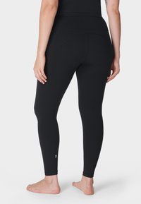 Zwarte high-waisted legging gemaakt van rekbare stof, met een slank ontwerp en subtiele logo-detail boven de enkel. Soepele textuur.