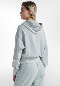 Lyseblå hættetrøje med afslappet pasform, kort længde og ribbede manchetter. Blød tekstur og syningsdetaljer ved kanten.