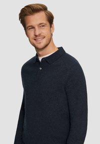 Marineblauwe gebreide pullover met kraag, voorzien van lange mouwen en een knoopsluiting. Zachte textuur, ontspannen pasvorm en een subtiele glans.