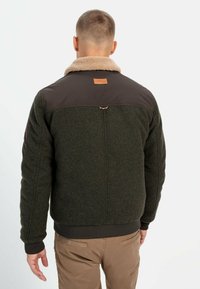 Men's jacket in dark green with a soft brown faux fur collar. Features quilted sleeves and a leather patch on the upper back.