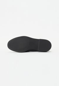 Schwarze Schuhsohle mit einer glatten, abgerundeten Form und horizontalen Rillen für besseren Halt. Entworfen mit einem minimalistischen Erscheinungsbild und aus langlebigem Material.