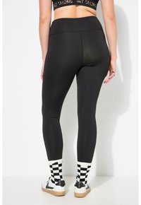 Leggings neri con una trama liscia e elasticizzata, vita alta, abbinati a calzini a scacchi bianchi e neri e scarpe sportive.