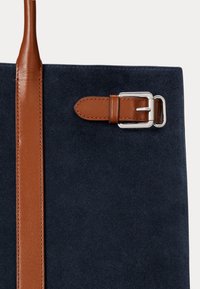 Námornícky semišový tote bag s hnedým koženým popruhom, s striebornou kovovou sponou ako akcentom. Jednoduchý, štruktúrovaný dizajn.
