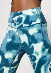 Leggings a vita alta in un motivo astratto blu e verde, realizzati in un tessuto liscio ed elastico. Presentano una tasca laterale e cuciture piatte.