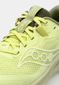 Chaussure de course vert clair avec une tige en maille texturée, une languette rembourrée et des accents vert foncé contrastants. Équipée de lacets jaunes vifs et de détails de logo.