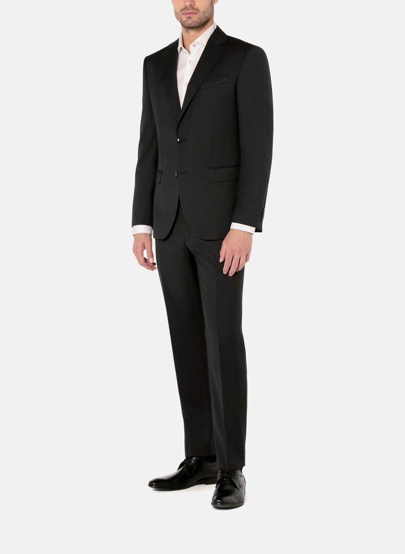 Schwarzer maßgeschneiderter Anzug mit Reverskragen, zwei Knöpfen und Taschen. Darunter ein weißes Hemd. Schwarze Lederschuhe. Glatte Stoffoberfläche.