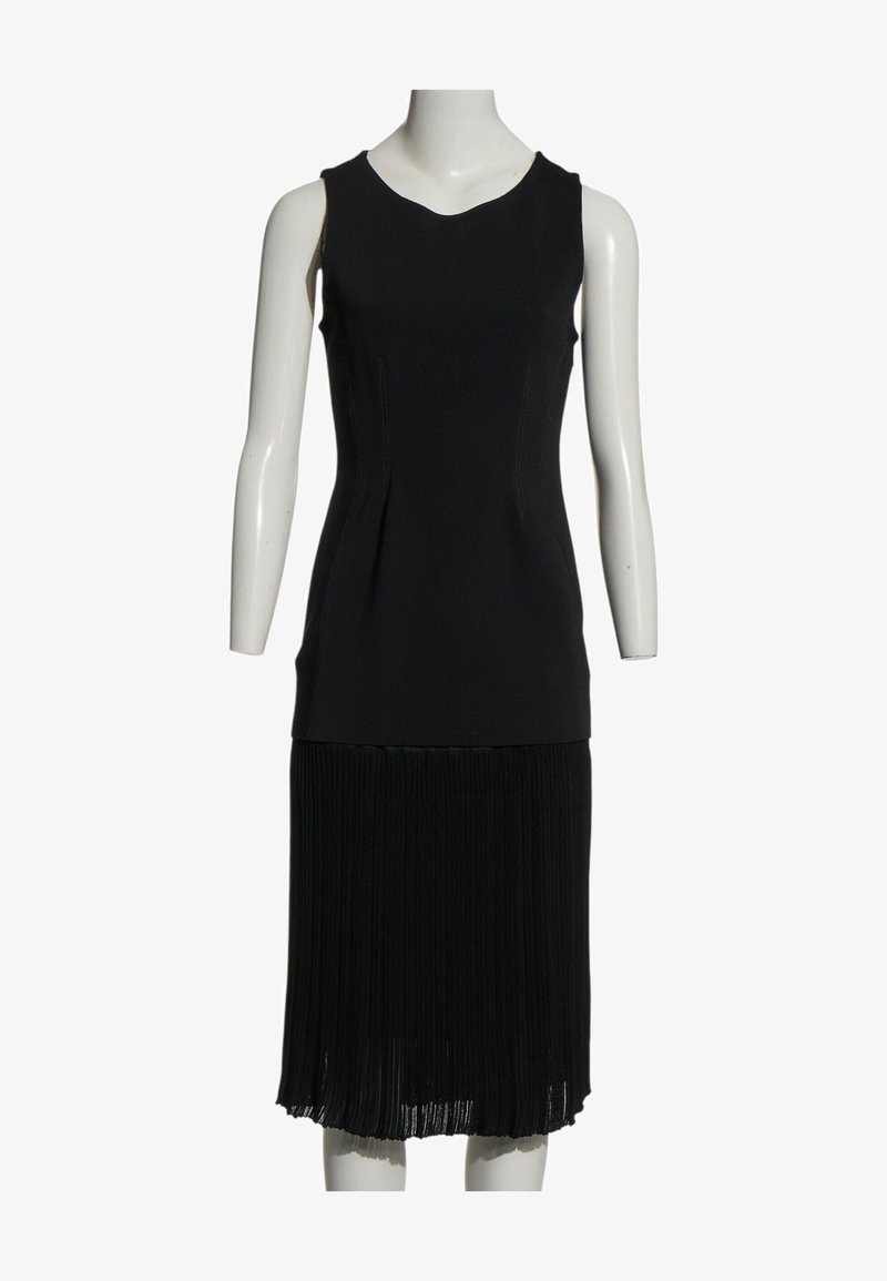 Robe noire sans manches avec haut ajusté et détail de jupe plissée présentée sur un mannequin blanc sur fond blanc.