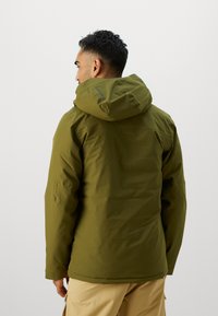 Jachetă impermeabilă verde măslin cu glugă, manșete elastice și croială dreaptă. Textură netedă, branding minim și fără modele vizibile.