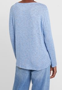 Ljusblå tröja med ett strukturerat stickmönster, med en avslappnad passform, långa ärmar och en rundad nederkant bak. Kombinerad med denimbyxor.