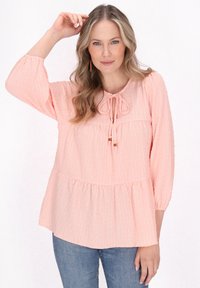  ferskenfarvet bluse med trekvartærmer, rund hals og bindedetalje fortil, som har en samlet peplumkant.