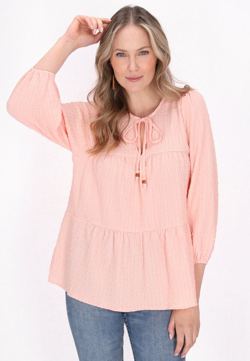  ferskenfarvet bluse med trekvartærmer, rund hals og bindedetalje fortil, som har en samlet peplumkant.