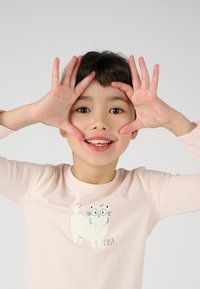 Chemise à manches longues rose clair avec une illustration de chat en dessin animé portant des lunettes et le mot "COSY". Texture douce et design simple.