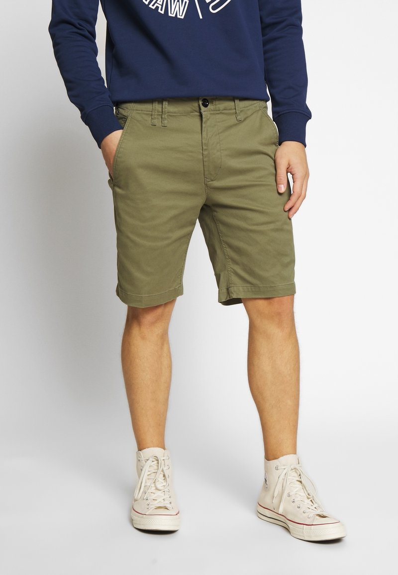 Gröna bomullsshorts med rak skärning, sidofickor och upprullade fållar. Bärs med en marinblå tröja och beiga hög-top sneakers.