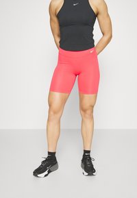 Jasnoróżowe sportowe szorty z gładkiego, elastycznego materiału, z wysokim stanem i kontrastowym logo Nike. Ubrane z czarnym topem na ramiączkach i czarnymi trampkami.