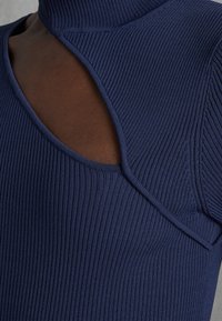 Marinblå ribbad topp med hög krage, utskärning på axeln och slät yta med en nära passform.
