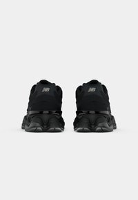 Baskets noires avec un dessus texturé, présentant une semelle intermédiaire brillante et un design de semelle légèrement incurvé. Logo New Balance en gris sur le talon.