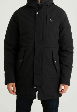 Homme portant un manteau d'hiver noir à capuche avec fermeture éclair frontale, fermeture à boutons-pression et plusieurs poches avant.