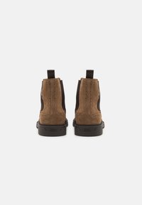 Botine din suede maro, cu panouri laterale elastice, accesorii metalice, vârf rotund și talpă din cauciuc negru. Viziune din spate prezentată.
