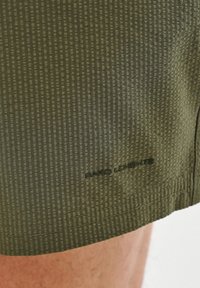 Olivkowe szorty z teksturowanym, pionowym wzorem w paski. Posiadają mały czarny napis logo na końcu. Materiał wydaje się lekki i przewiewny.
