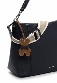 Sort læderhåndtaske med tekstureret finish, med en beige og grå stribet rem og en bamsevedhæng. Sølvfarvede metaldele.