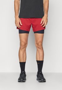 Red and navy shorts with an inner lining, paired with black socks and running shoes. Simple design, fabric appears lightweight and smooth.
