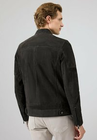 Zwarte leren jas met een gladde textuur, voorzien van een staande kraag, zijritsen en een getailleerd ontwerp. De achterzijde toont naaddetails.