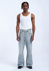 Jasnoniebieskie dżinsy z szerokimi nogawkami o wyblakłym wykończeniu, z pięcioma kieszeniami i zapięciem na guzik, noszone z białym topem na ramiączkach.