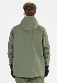 Lätt, vattenavvisande jacka i olivgrön med huva, som har en avslappnad passform och elastiska ärmslut. Svarta handskar synliga vid ärmarna.
