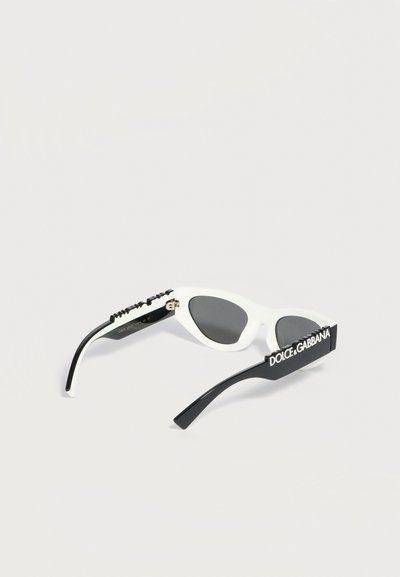 Λευκά και μαύρα γυαλιά ηλίου cat-eye με σκουρόχρωνους φακούς, με το λογότυπο "Dolce & Gabbana" σε λευκό σε έναν μαύρο βραχίονα.