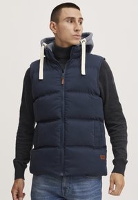 Navy puffer vest with a zip front and gray hoodie. Features hood drawstrings, horizontal stitching, and a logo on the chest.