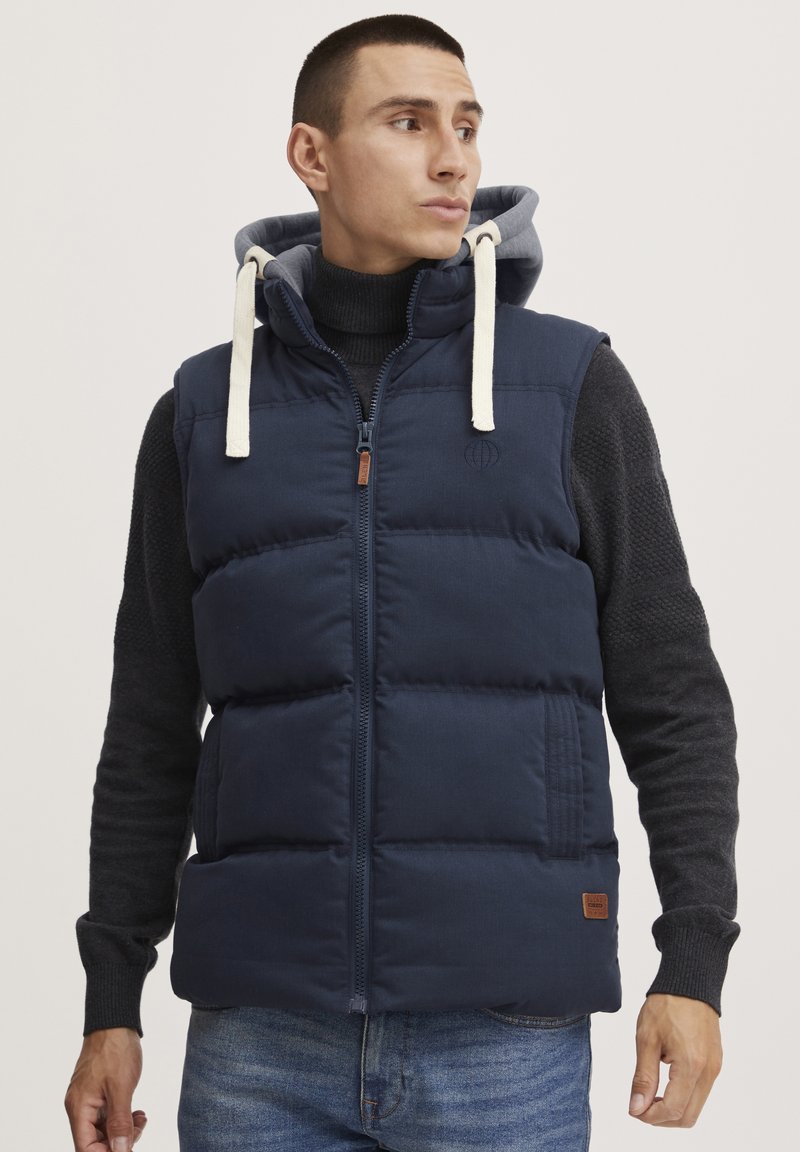 Navy puffer vest with a zip front and gray hoodie. Features hood drawstrings, horizontal stitching, and a logo on the chest.