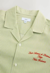 Chemise à col rayée vert clair et blanc avec des boutons et un texte rouge brodé indiquant « Sant Antoni de Portmany Ibiza Illes Balears ».