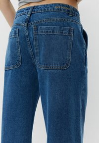 Vaqueros de denim azul con cintura alta, que cuentan con dos bolsillos traseros y detalles de costura sutiles. Nombre de la marca "SOFIE SCHNOOR" grabado en la cinturilla.