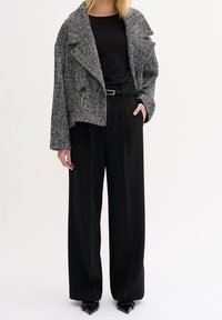 Svart och vit houndstooth-mönstrad kavaj, oversized passform, med en svart topp och högmidjade svarta byxor, kompletterat med spetsiga svarta skor.