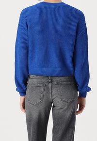 Maglione lavorato a maglia blu con design cropped e finitura testurizzata. Presenta maniche lunghe e orlo a coste, abbinato a jeans grigi.