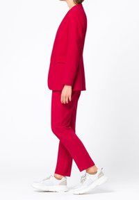 Completo su misura rosso con maniche lunghe e pantaloni a gamba dritta, abbinato a scarpe da ginnastica bianche. Texture liscia, design minimale e senza motivi visibili.
