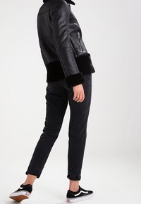 Svart läderjacka med pälsdetaljer, kombinerad med mörka jeans och svarta och vita sneakers. Har en dragkedjeficka och en figurnära design.