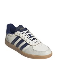 White leather sneakers with navy blue stripes, textured accents, and a gum rubber sole. Features white laces and perforated toe detail.