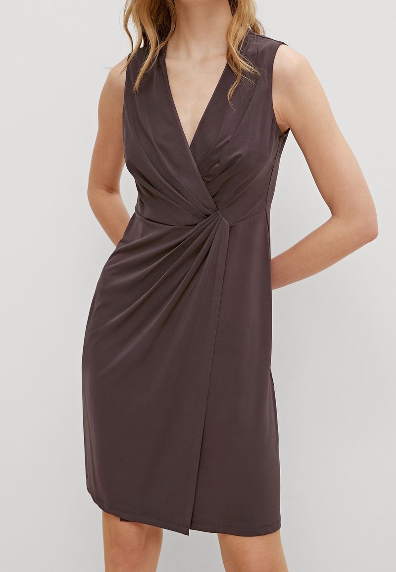 Robe sans manches marron foncé longueur genou avec décolleté en V et drapé froncé sur un côté, portée par une personne debout.