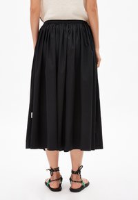 Schwarzer, knielanger Rock mit gerafftem Taillenbund. Aus leichtem Stoff gefertigt, mit einer glatten Textur. Dazu passende schwarze Sandalen mit geflochtenen Riemen.