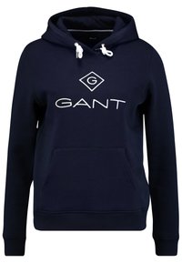 Felpa con cappuccio blu navy realizzata in morbido tessuto. Presenta un grande logo bianco "GANT" e una tasca a marsupio frontale. I lacci sono bianchi.