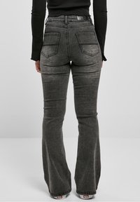 Vaqueros acampanados en mezclilla gris oscuro con un acabado desteñido. Cuenta con dos bolsillos traseros y un diseño de cintura alta.