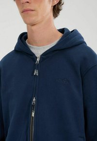 Felpa con zip di colore blu navy, con cappuccio foderato, tasche frontali e logo tonale sul petto. Realizzata in un morbido tessuto misto cotone.