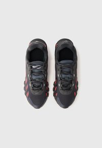 Um par de ténis atleticos pretos e vermelhos com atacadores, vistos de cima sobre um fundo branco.